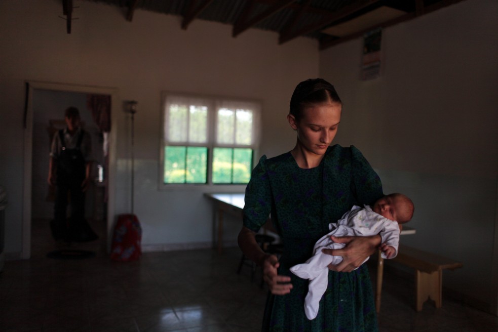 Mennonite teenager Maria, 15, holding a newborn baby in her home