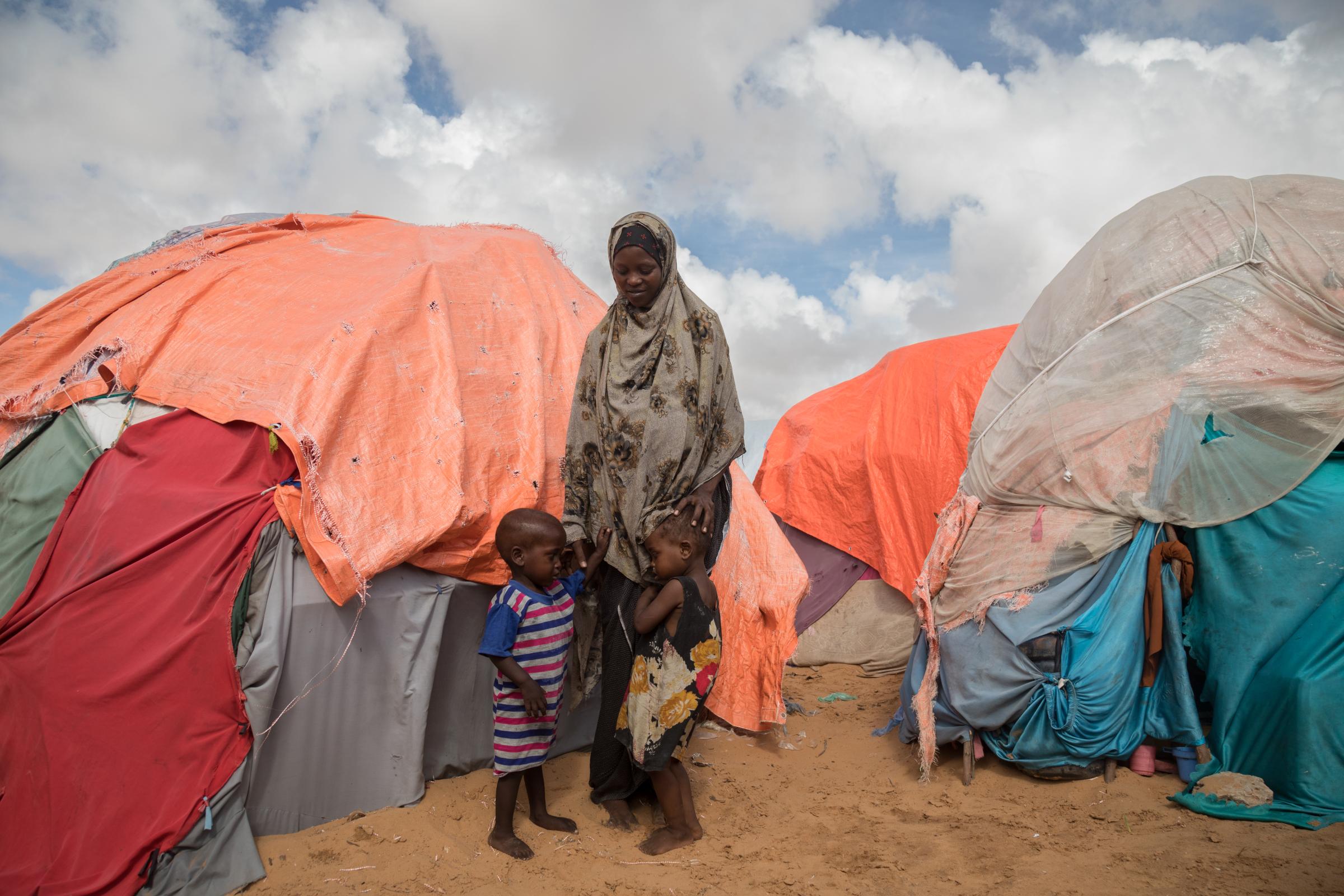 Facing the Dual Crisis: A Glimpse into the Lives of Women and Children in Somalia's Kahda District IDP Camp - Luul Mustaf, a resilient twenty-year-old mother, stands with her two young children, aged 3 and...