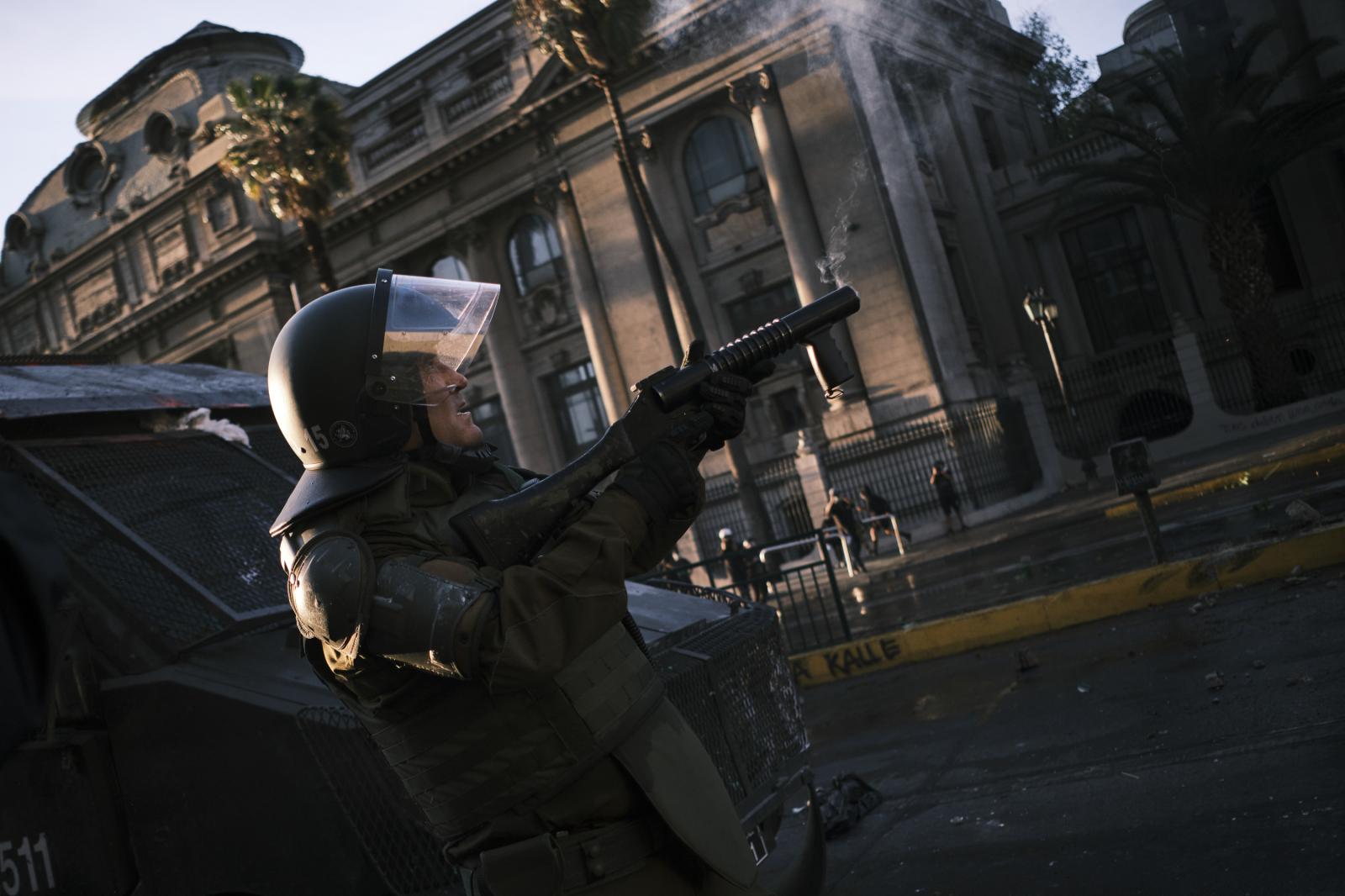 Image from CHILE: From politics to social unrest. - Un carabinero dispara una bomba de gas lacrimogeno hacia...