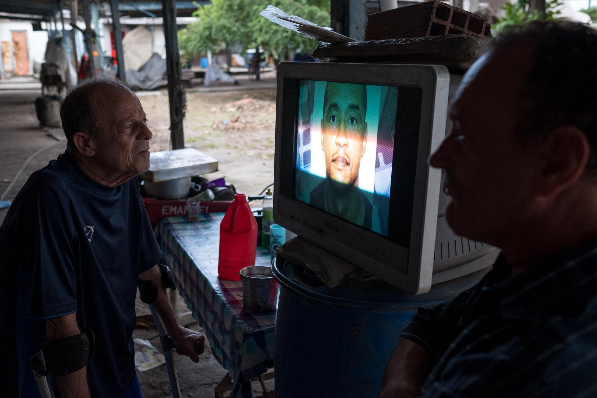 Baía Viva - Fishermen listen close to the television for a report on...