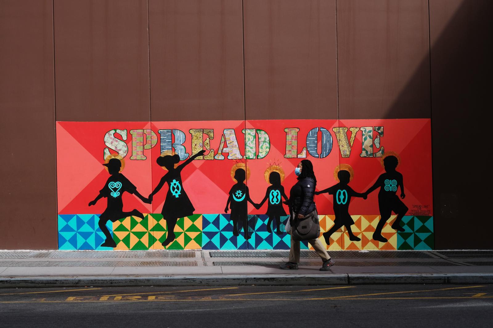 Women in surgical mask walks in... "Spread Love" mural.
