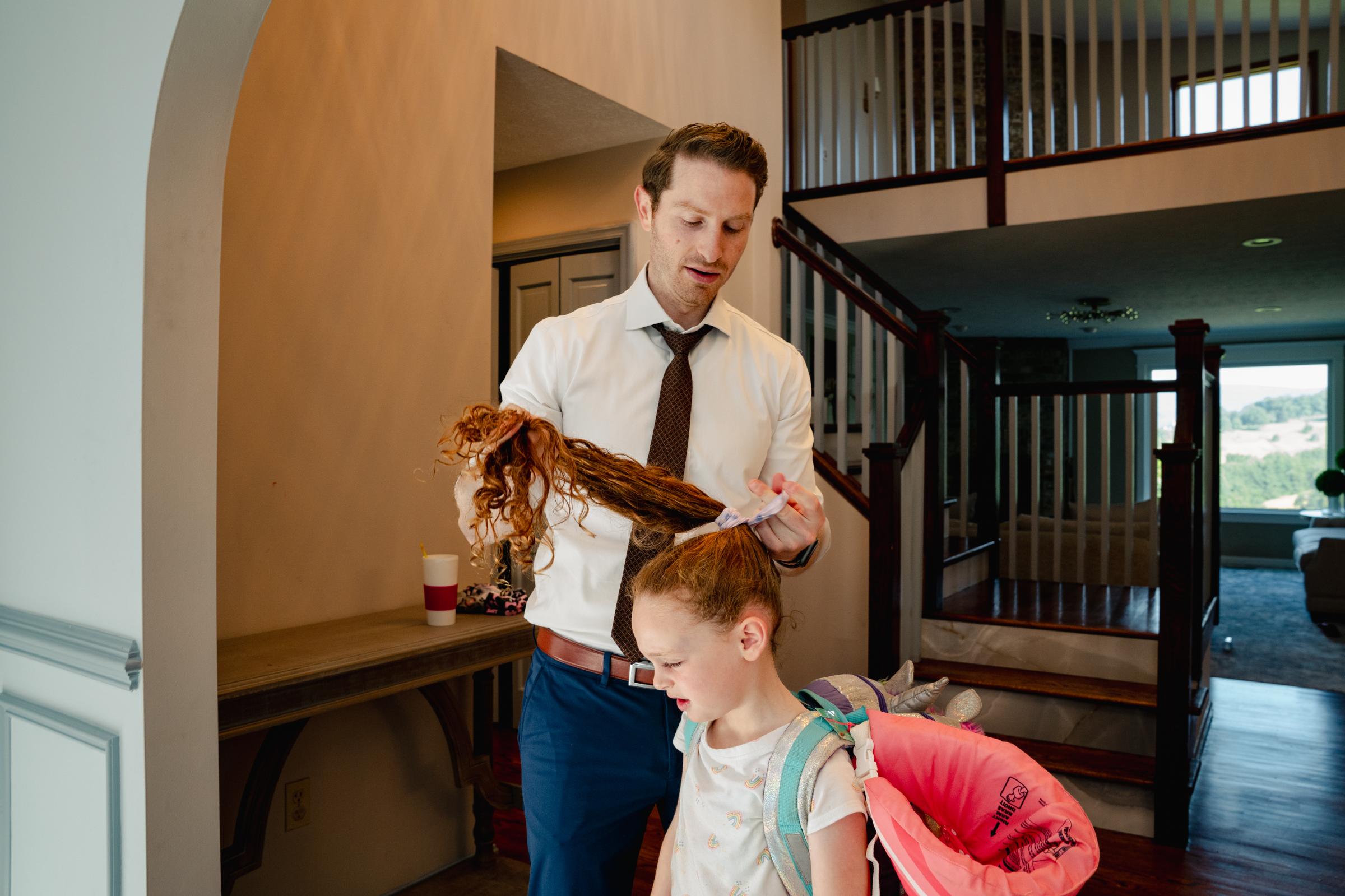 Working Parents Are Having a Rough Summer. Some Co-Workers Don’t Want to Hear About It. -  Eli Albrecht ties his daughter Paz's hair before she...