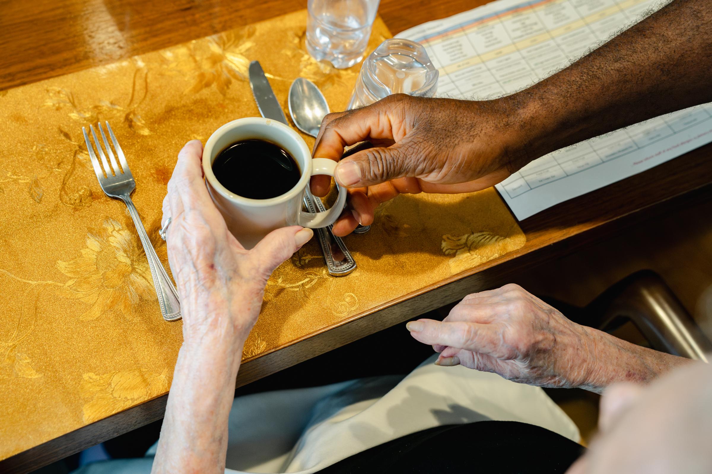 The Crisis Facing Nursing Homes, Assisted Living and Home Care for America’s Elderly -  Momah Walopaye brings coffee to a resident at Goodwin...