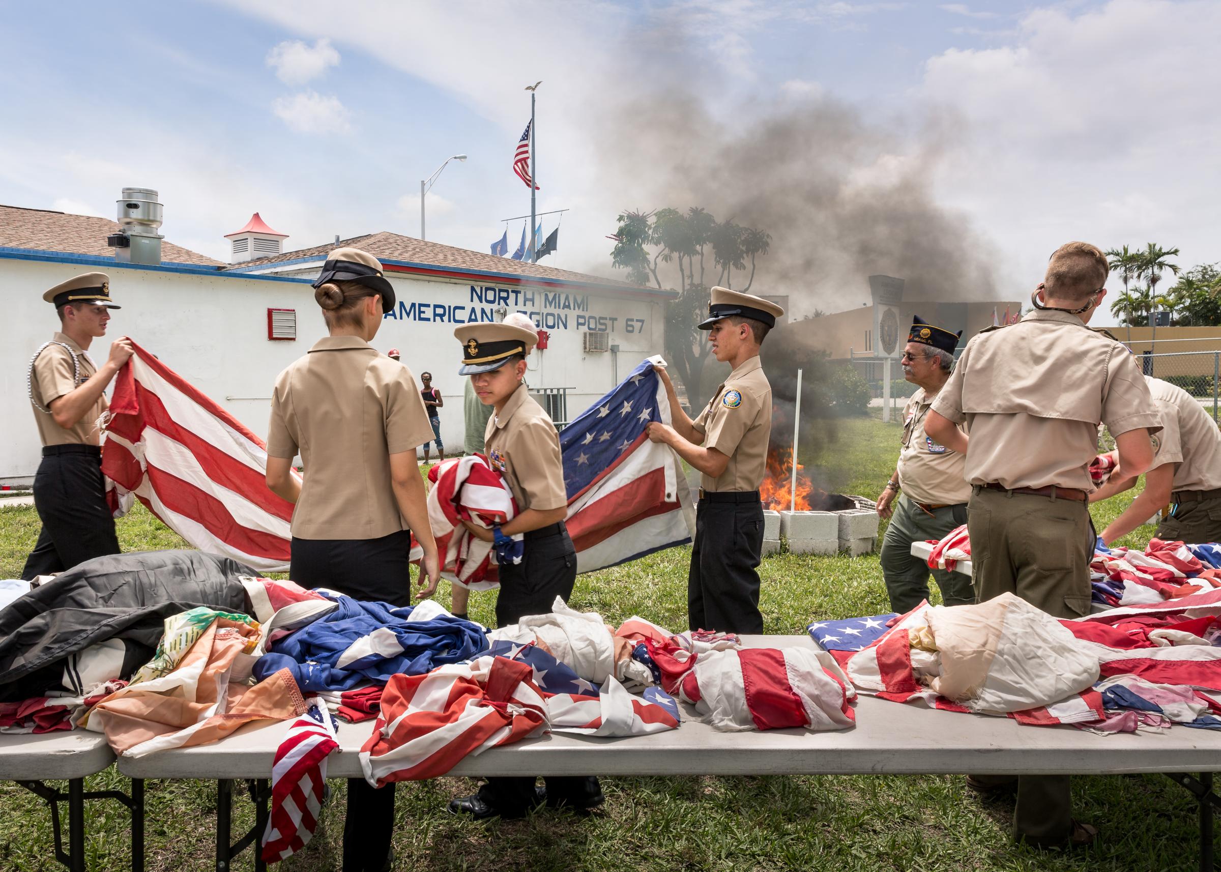 Post 67 - Members of the Navy JROTC and Boy Scout Platoon 406 work together to prepare flags at the annual...
