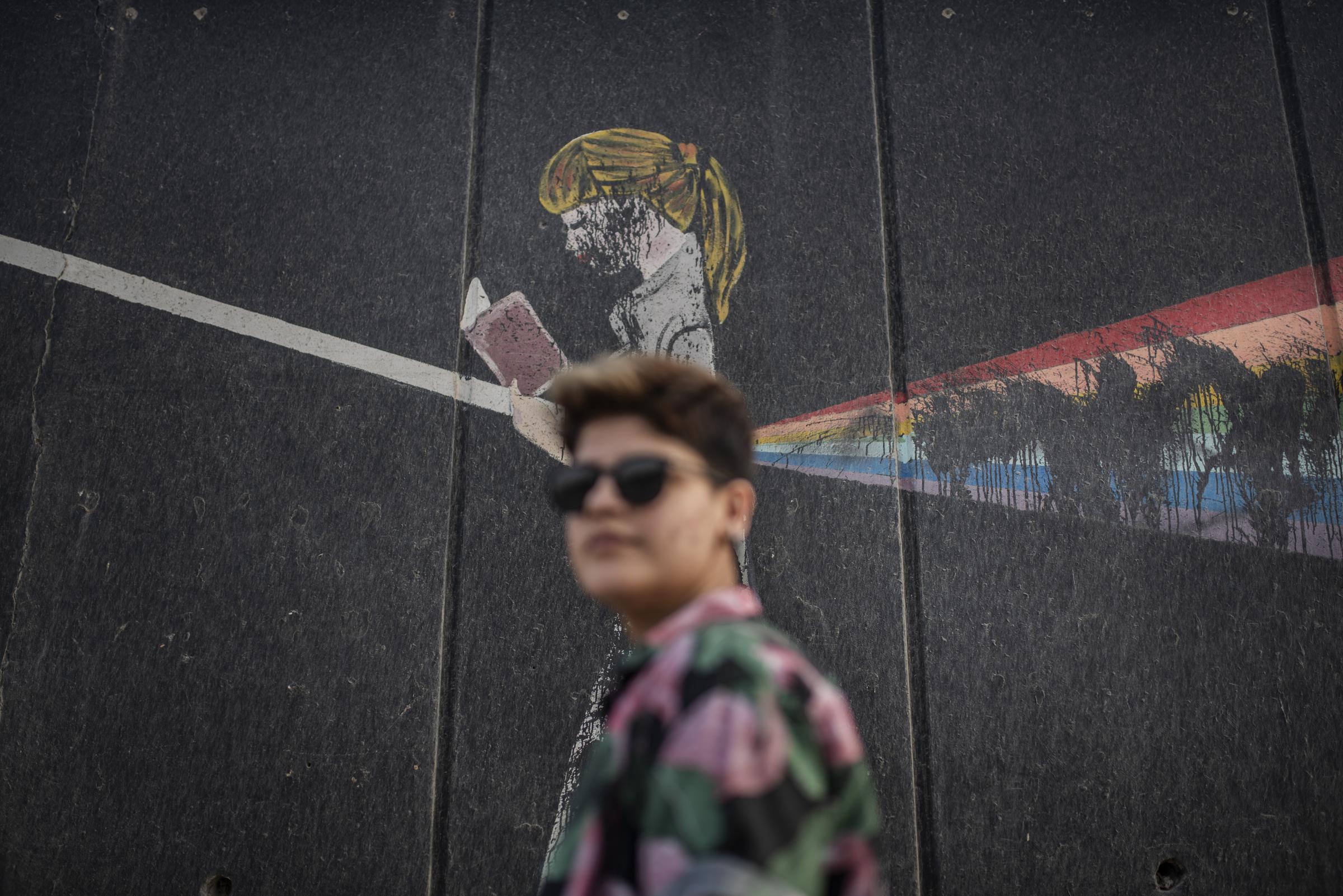 Queer in Iraq - R in front of a graffiti with the homosexual flag that...