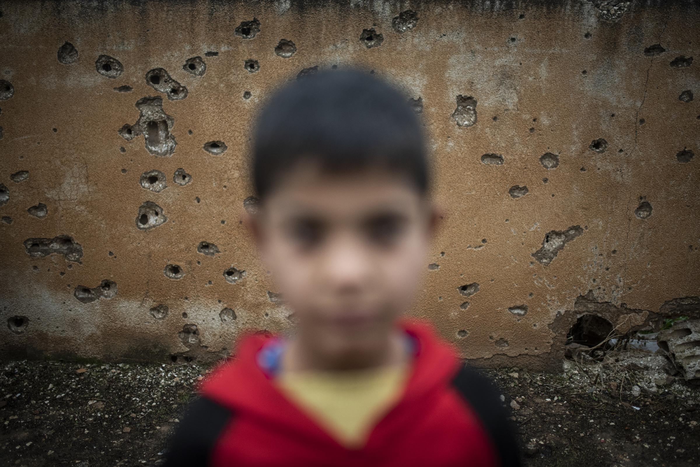 Mud Swings In Fire Fields - A portrait of a boy in front of a holed by bullets wall...