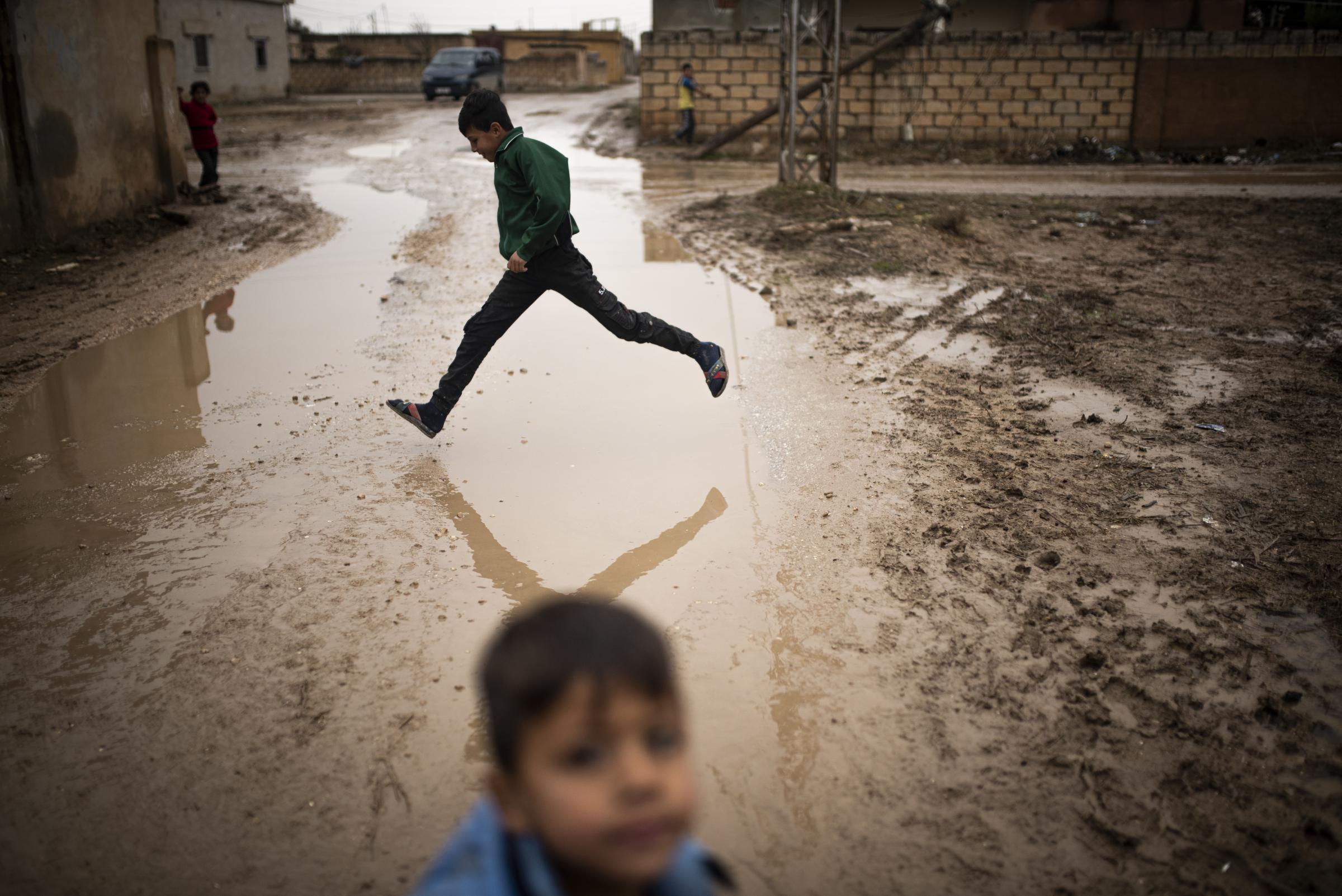 Mud Swings In Fire Fields - A child jumping a puddle in a street of Tel Nasri near...