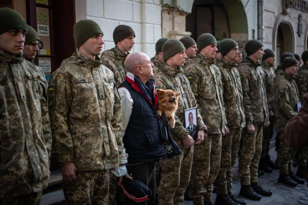 Image from Ukraine - A man with a dog stands amidst soldiers at the funeral...