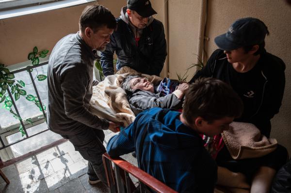 Image from Ukraine - Volunteers carry a disabled woman in a stretcher down the...
