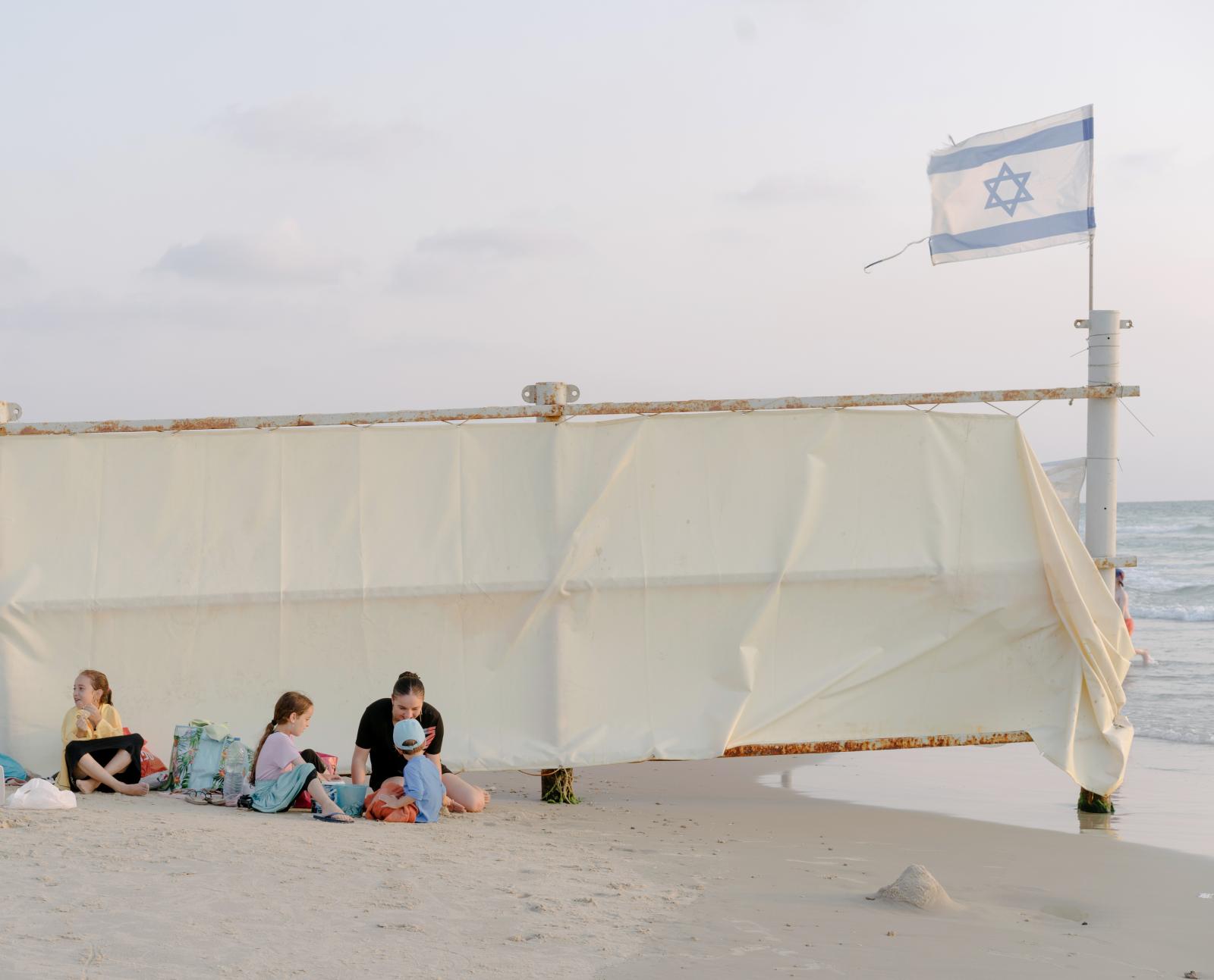  A family sitting by a sheet of...h the Israeli flag is hoisted. 