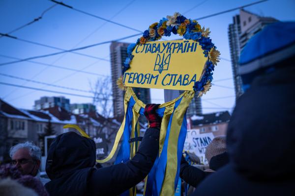 Image from [Ongoing] Ukrainian Toronto Protests - A woman protestor holding a flowered sign saying...
