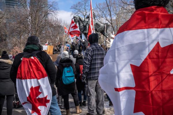 Protestors wearing Canadian flags listen to rally speakers. Trucker convoy protesters gather in Queen’s Park, Toronto for the second consecutive weekend in solidarity with anti-mandate demonstrations on February 12, 2021. It comes after the province declared a state of emergency in relation to the ongoing blockades, with Toronto police setting up road closures across the city.