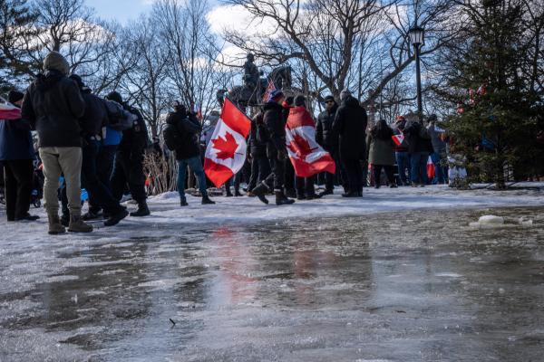 [2021] Anti-Mandate Protests - A man holding two Canadian flags walking across an icy...