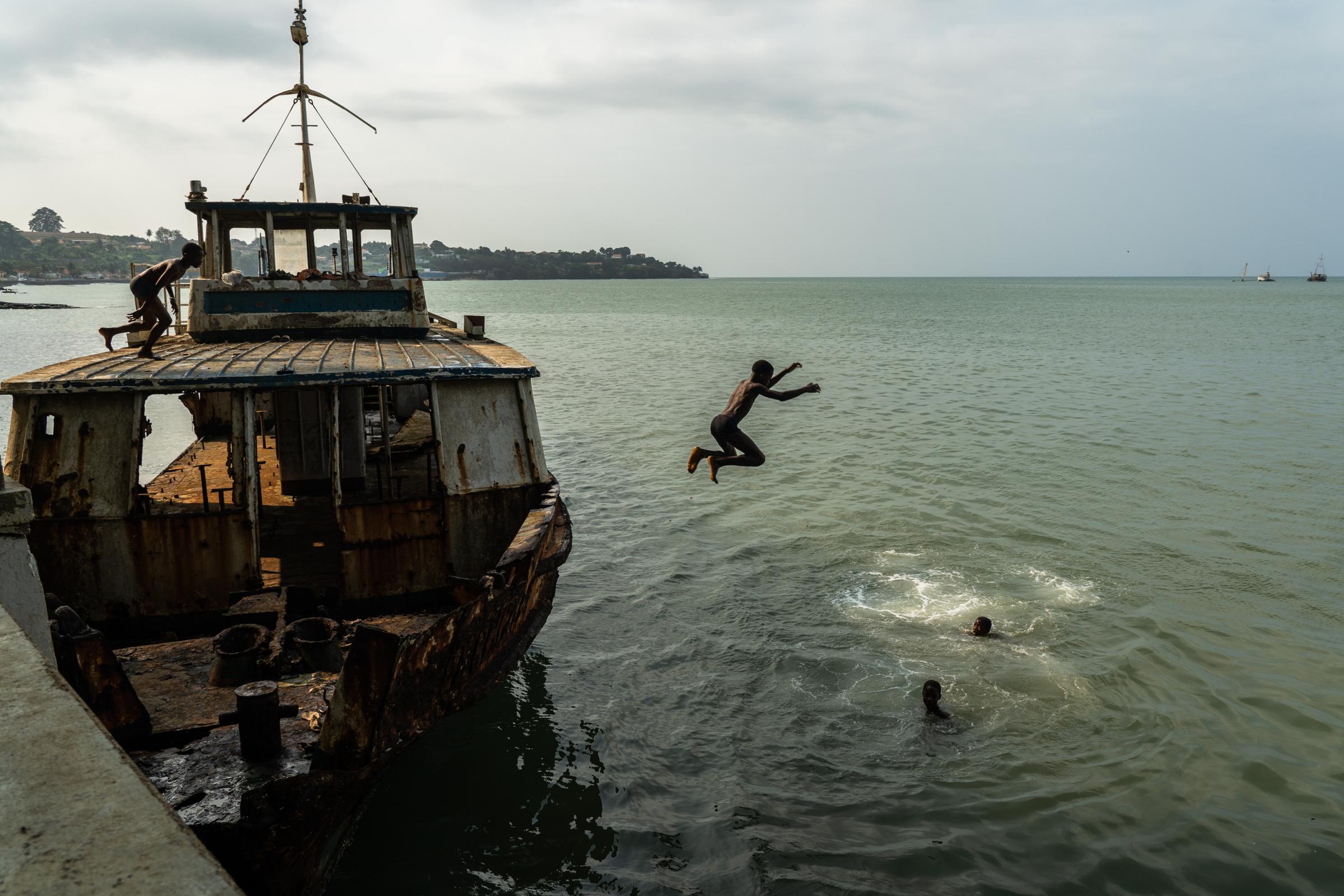 Genetic Engineering In the Mosquito War - Kids jump off the abandoned rusty boat into the bay in...