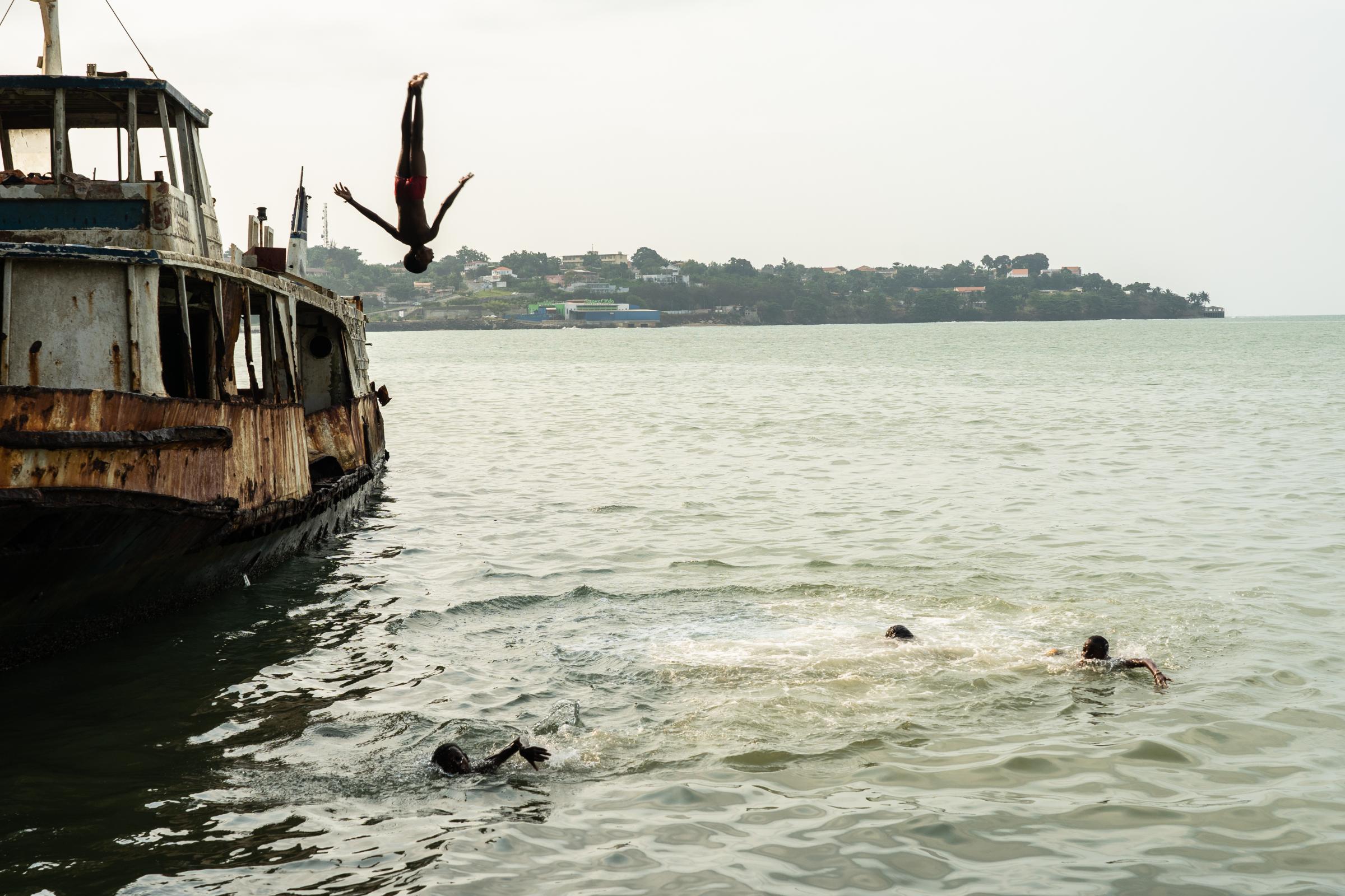 Genetic Engineering In the Mosquito War - Kids jump off the abandoned rusty boat into the bay in...