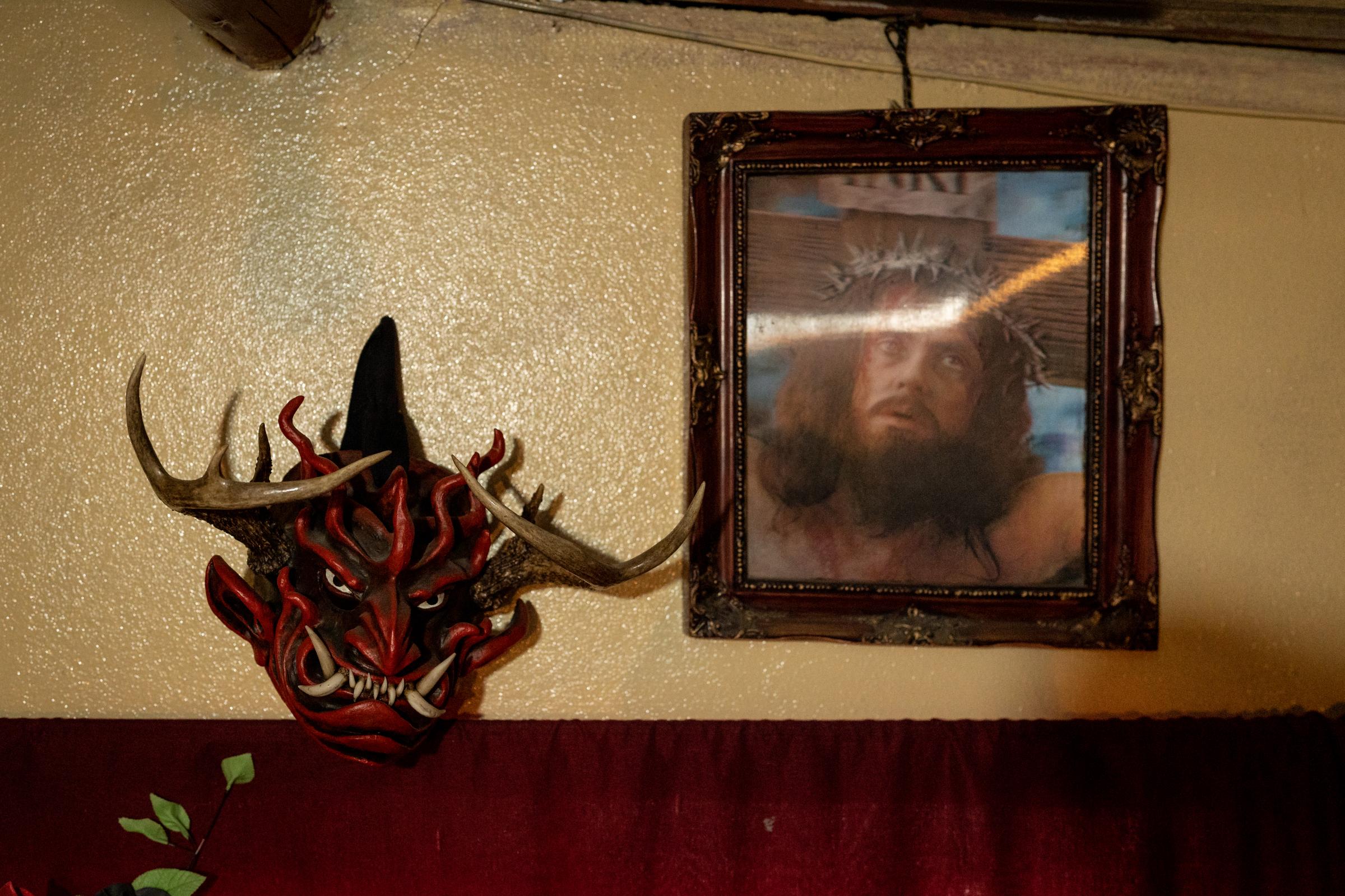 Los Diablos de Píllaro - A devil mask hangs next to a portrait of Jesus Christ at...