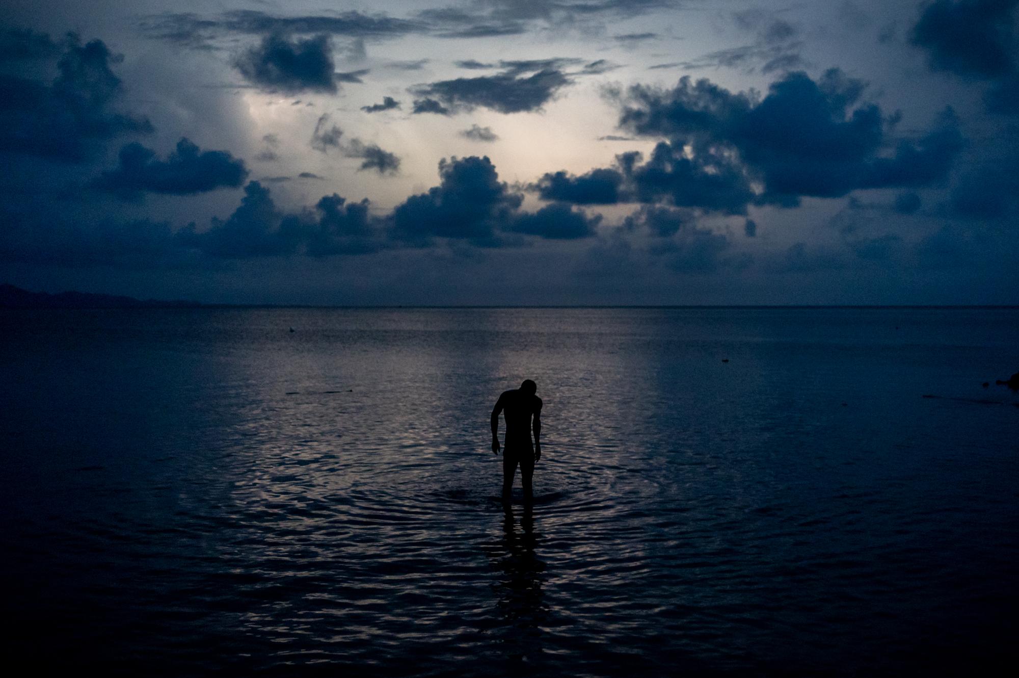 A Haitian migrant wades into the waters of the Gulf of Urab&aacute; as a lighting storm lights up the night sky across the gulf in...