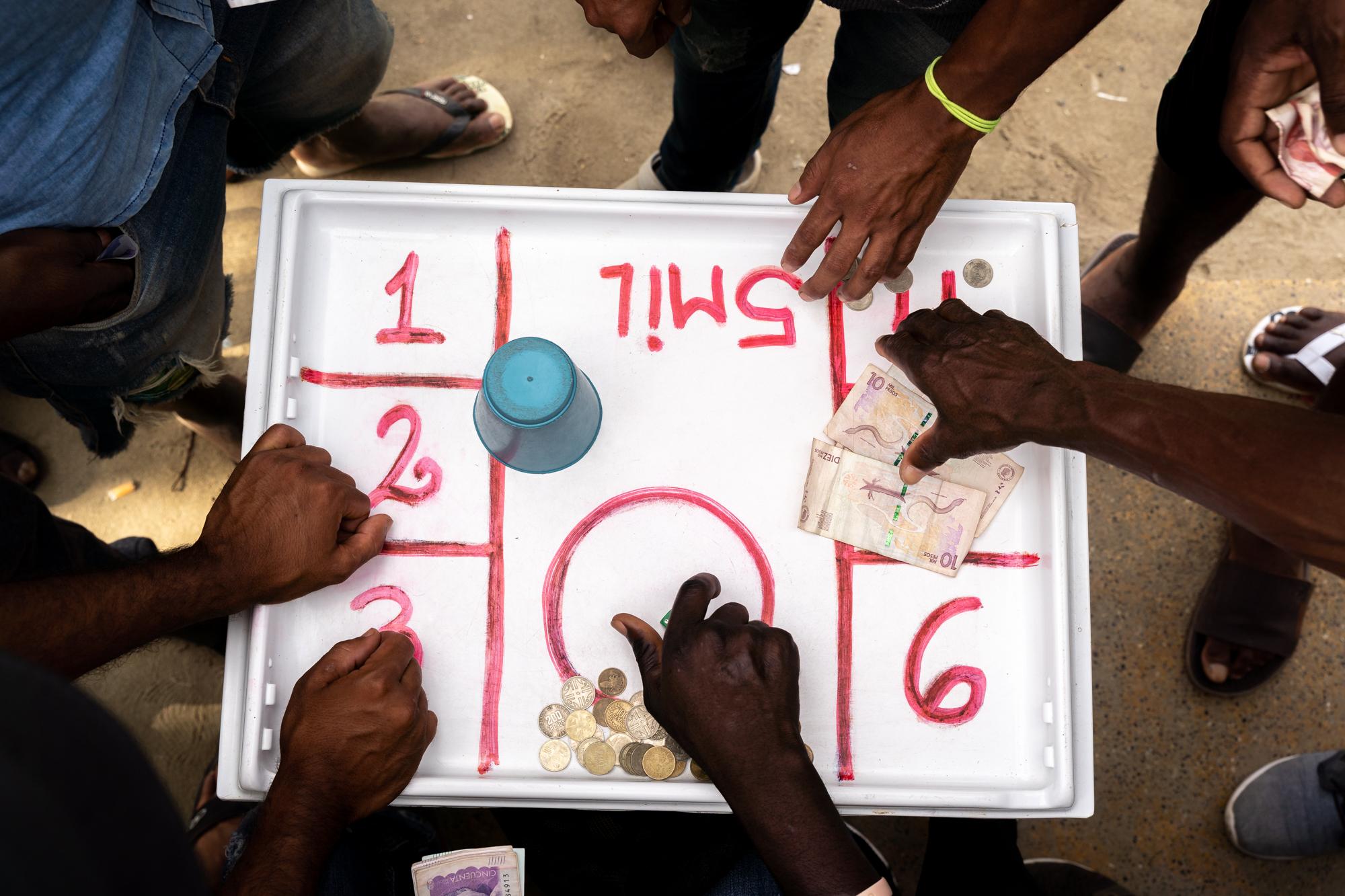 Inside The Derian Gap - Haitian migrants pass the time gambling on the beach in...
