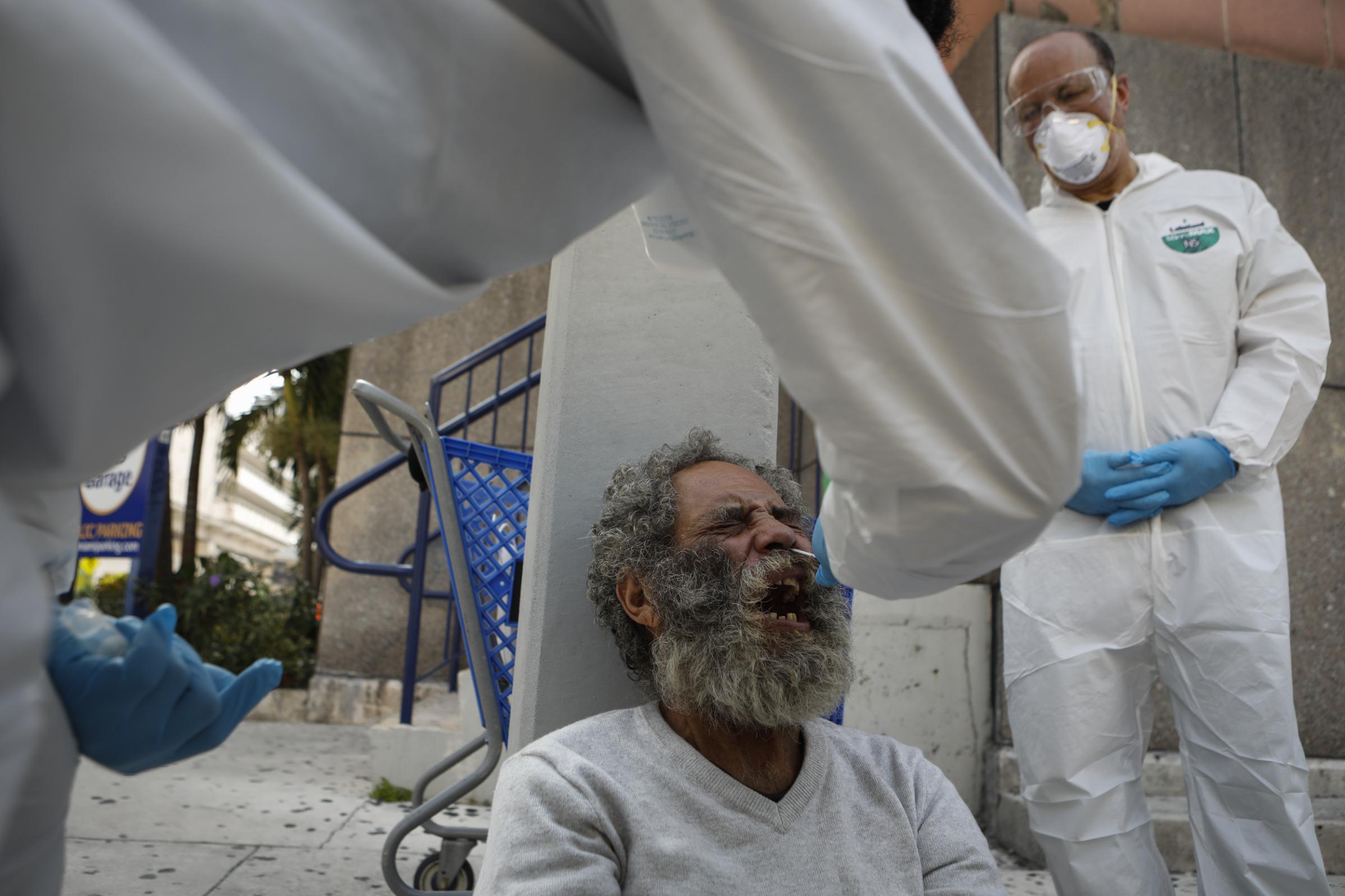 slideshow - A homeless man reacts as a worker uses a swap to collect a sample during a Miami-Dade County...