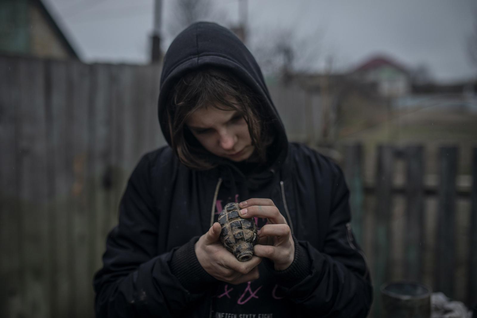 THE BUCHA MASSACRE - Ruslana, 10, holds a deactivated grenade outside her home...