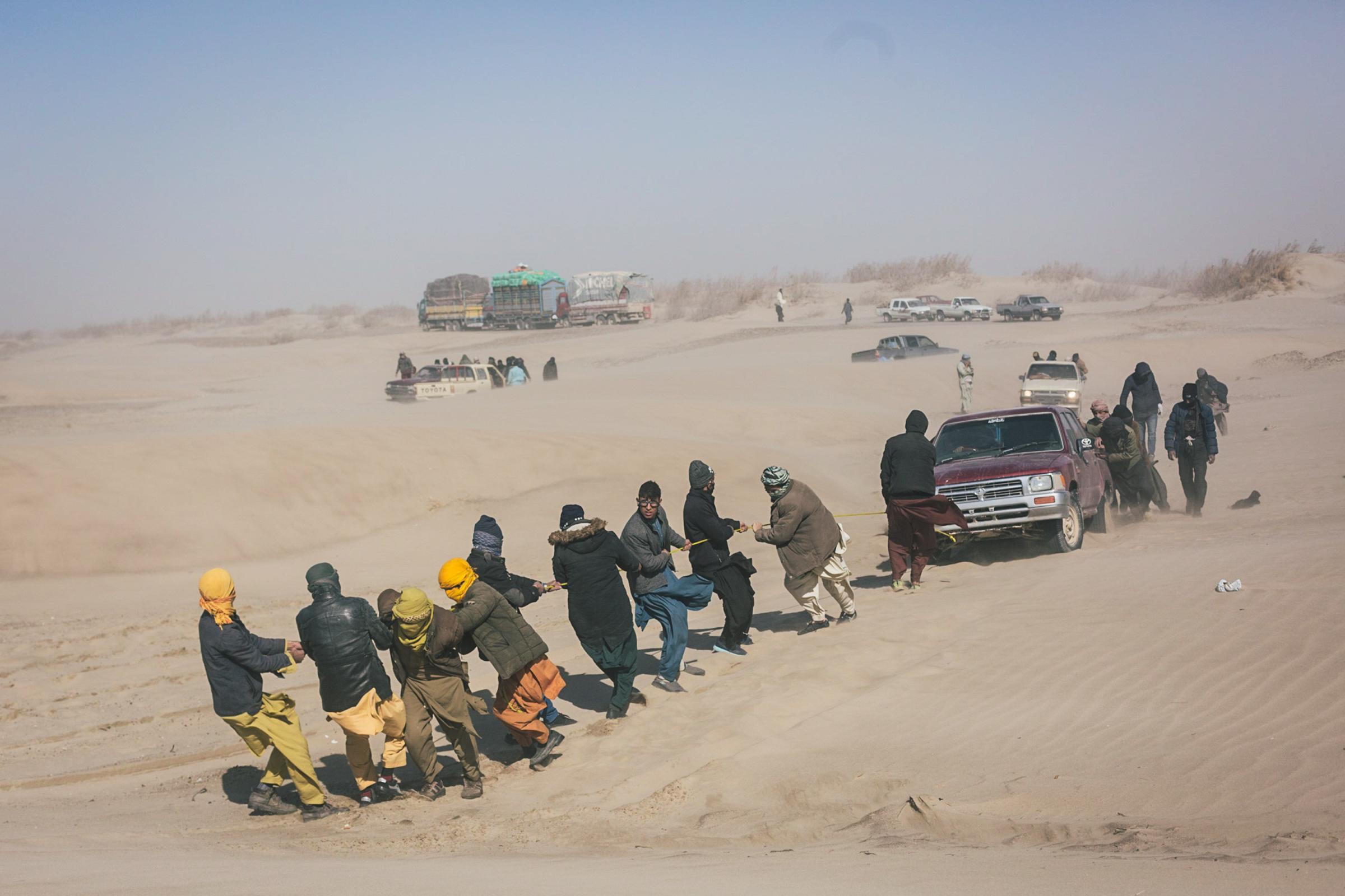 Afghan refugees pull pick-ups out of the desert sand.
