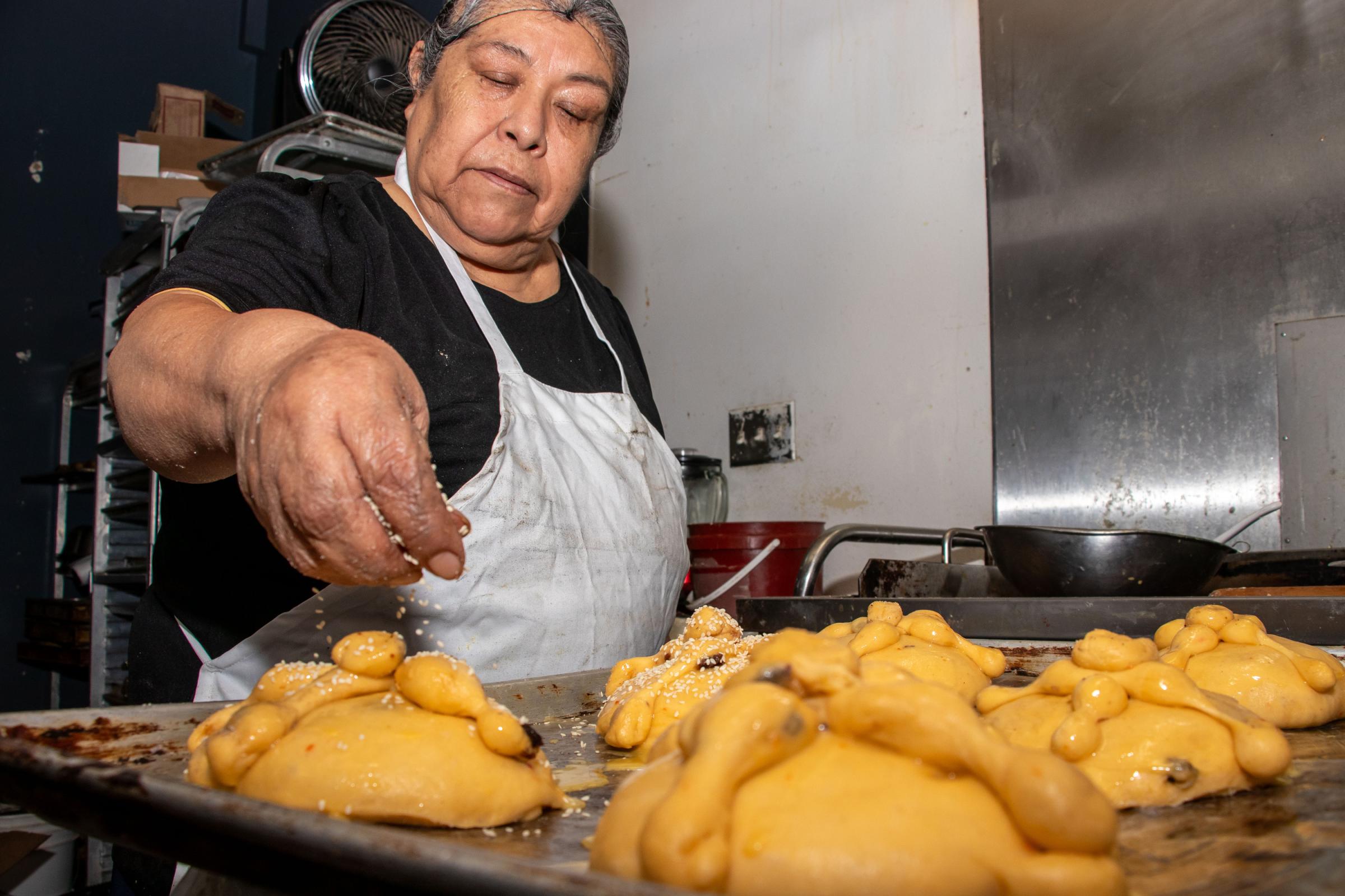 Dia de los Muertos - Eva Mejia tops Pan de Muerto with sesame seeds before...