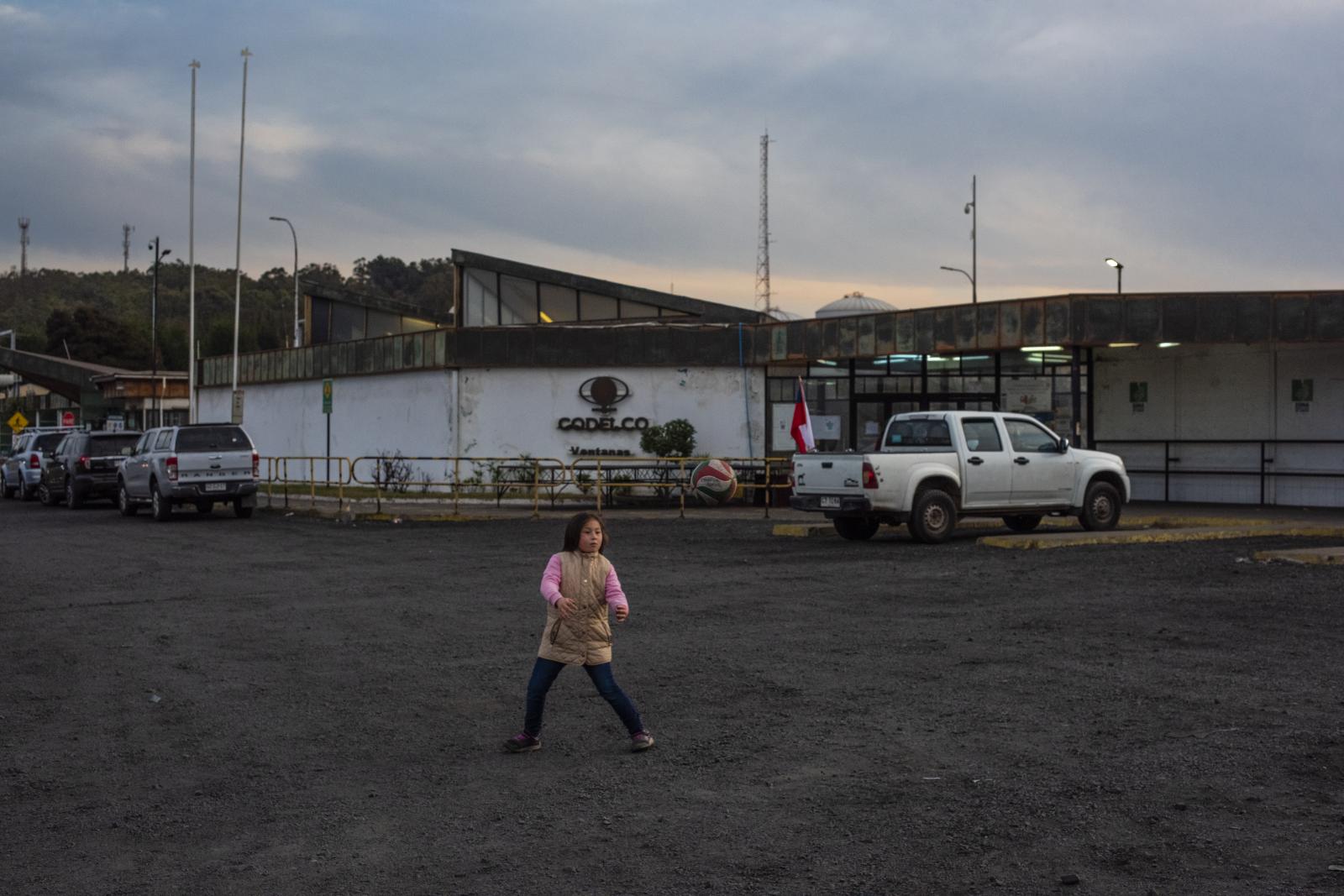 A girl plays ball at the entrance of the Codelco refinery factory. | Buy this image