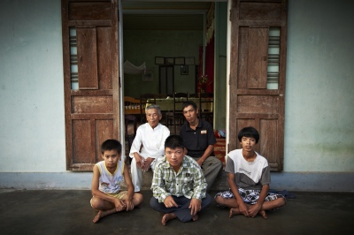  At a quick glance, they seem to be like any other families. But look closely and you will realize that there are three generations of victims of the Agent Orange in the family. The man dressed in white is the grandfather, Hoang Thang (Male, born in 1929), who got hit by the chemical in Hai Lang forest and to this day suffers from serious skin diseases and nervous system illnesses. His son, Hoang Van Danh (Male, born in 1977, top row on the right), has epilepsy with his right leg paralyzed, while his son, Hoang Anh Son (Male, born in 1983, eldest sonâ€™s son), is mentally challenged with paralysis on his right leg and foot. Second sonâ€™s son, Hoang Anh Duc (Male, born in 1994) is hearing impaired and mute. Lastly, third sonâ€™s son, Hoang Quang Tuong (Male, born in 2002) has epilepsy. The pain and sufferings inflicted by the Agent Orange, most unfortunately, are passed on from one generation to the next. (Dec. 7, 2012) 