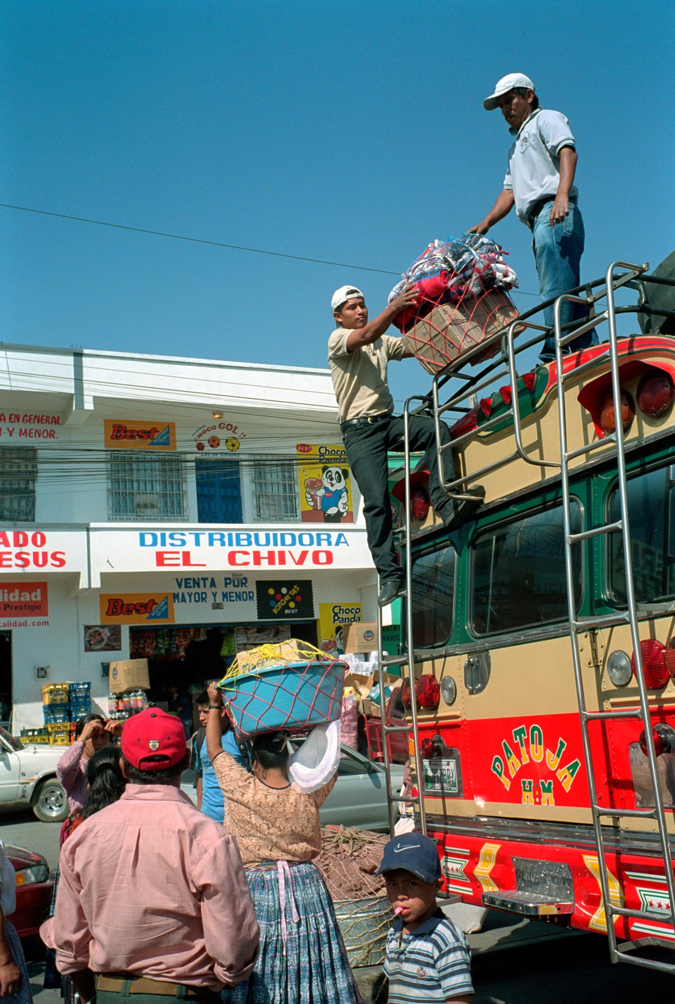With God and Ayudante Across Guatemala - Two  ayudantes  lift luggage from the roof of a bus at...