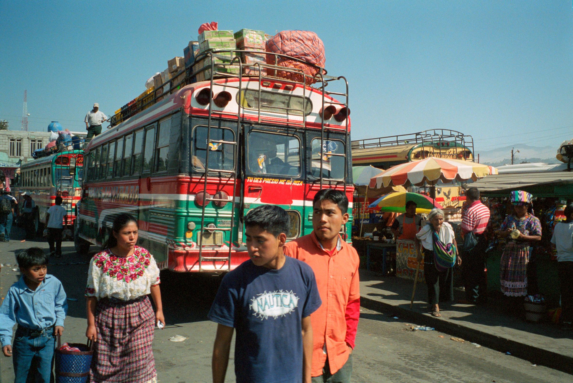 With God and Ayudante Across Guatemala - Passengers, fully loaded buses, and a street market at...