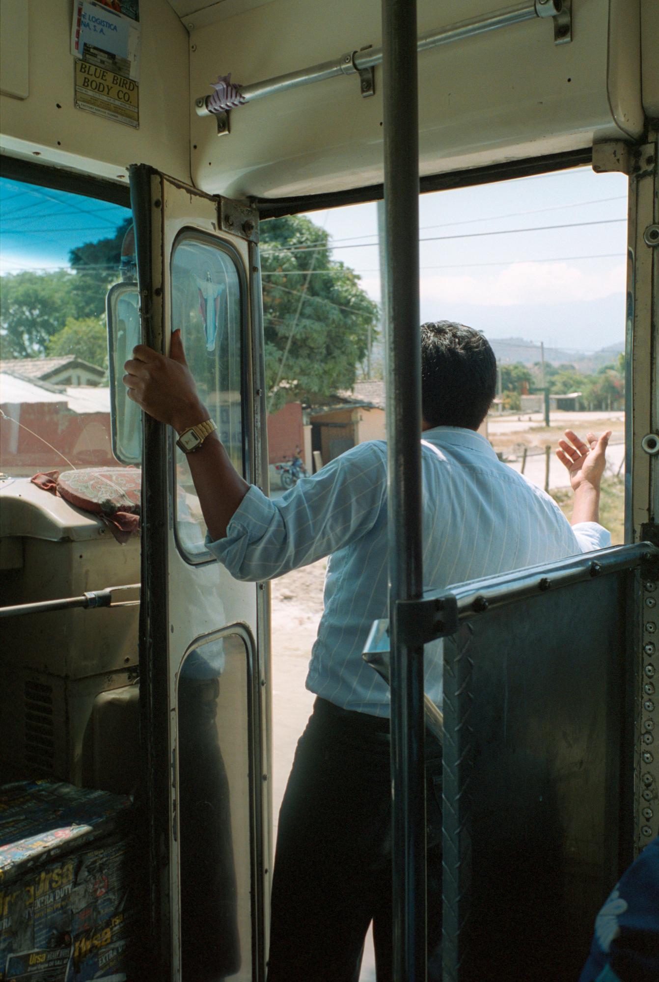With God and Ayudante Across Guatemala - An ayudante leans from the open doorway of his bus to...