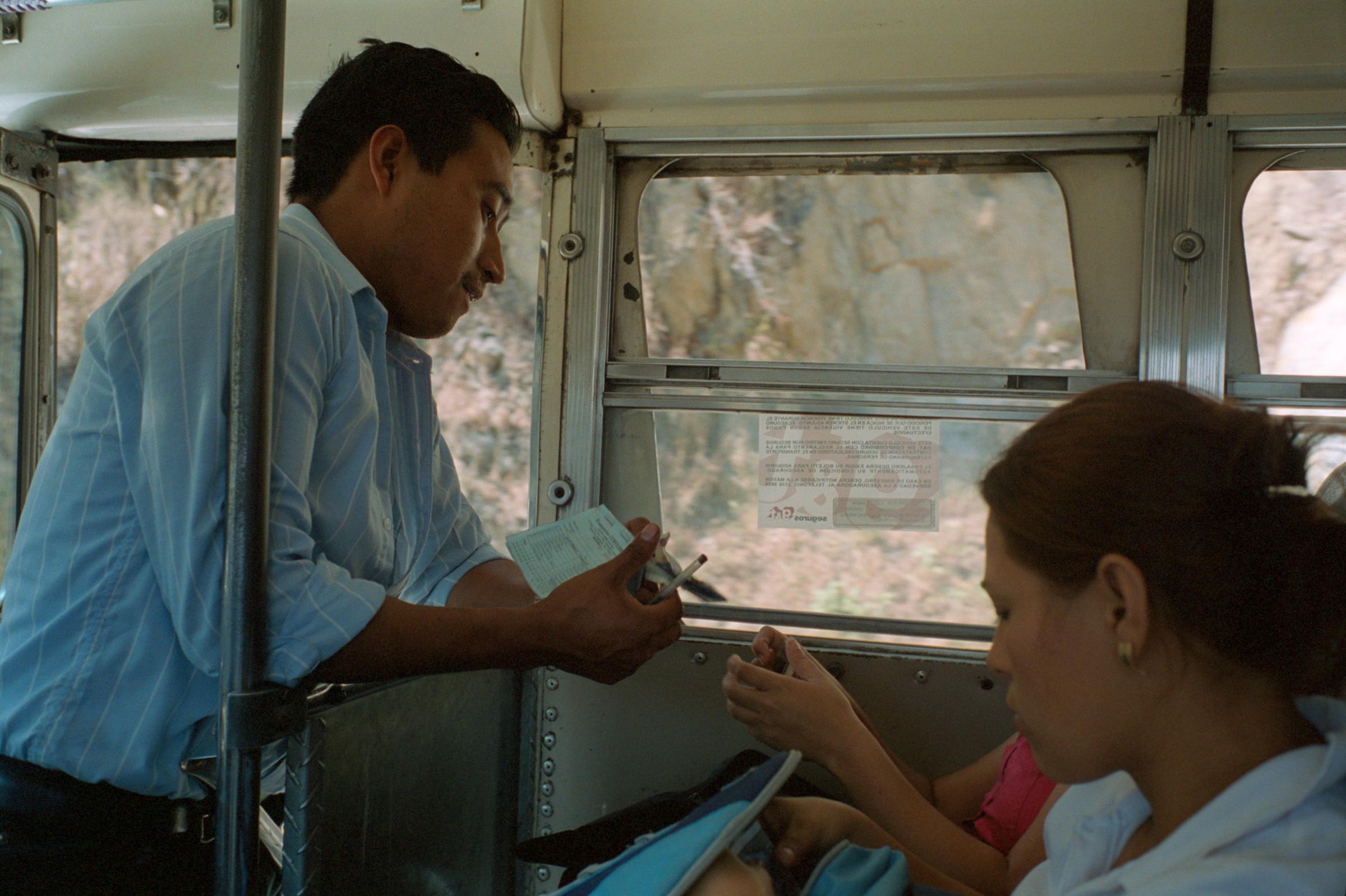 With God and Ayudante Across Guatemala - A bus assistant collects fares from passengers who have...