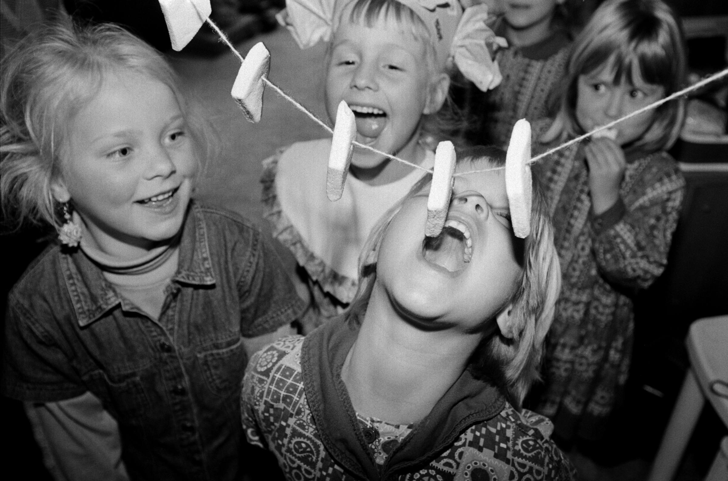Five girls play Bite the Marshmallow at the fifth birthday party of one of them. The birthday girl wears a paper crown. Linschoten, The...