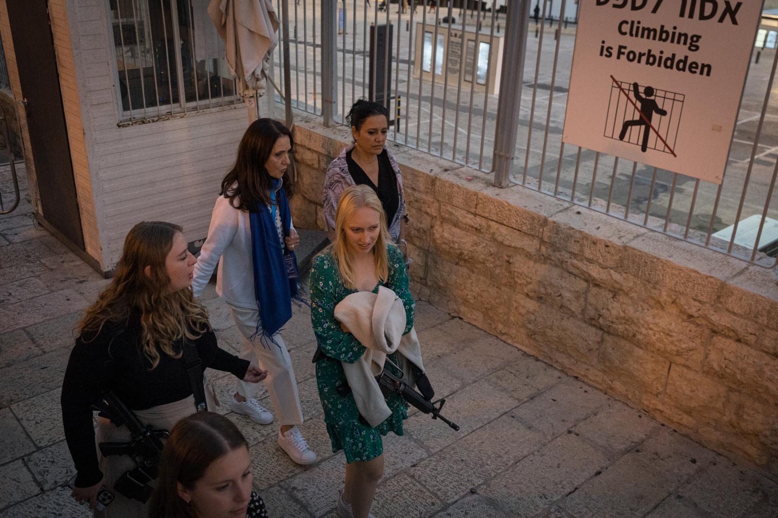 Israel, an announced war - A girl carries a gun hanging next to her friends on a Shabbat afternoon in Jerusalem.  