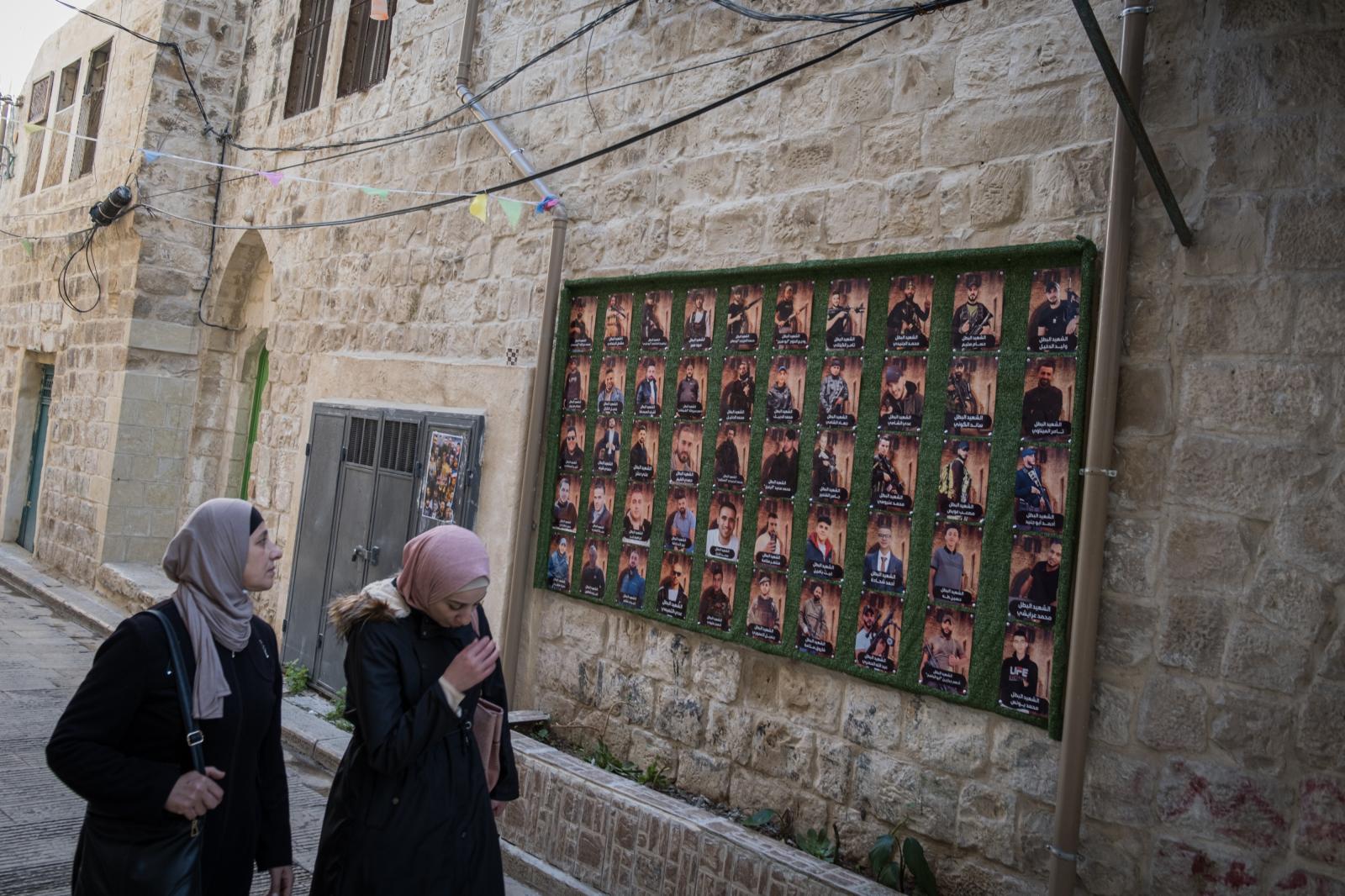 Israel, an announced war - Two women walk past a mural with photos of martyrs in the city of Nablus, Palestine.  