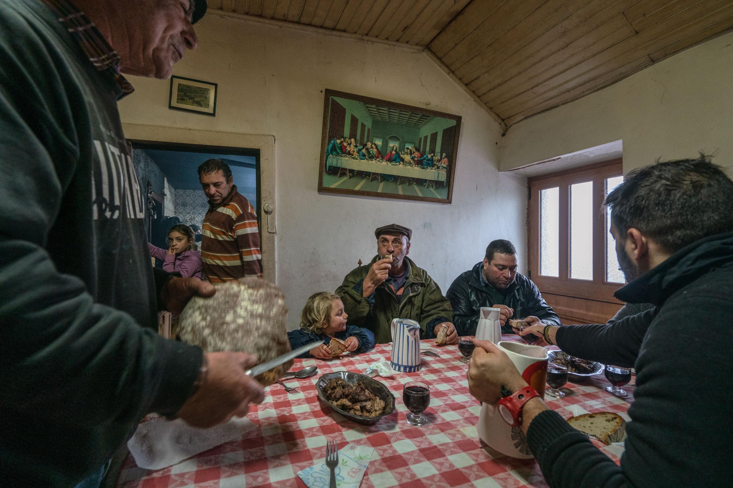 Vilarinho Seco, December 14th, 2019 - Elias Coelho (left) serves homemade bread to his family and neighbors after they all spent the morning slaughtering pigs outside his home in Vilarinho Seco. Every year, at the beginning of the winter, residents of villages in the Barroso region slaughter pigs to make ham and sausages that feed them all through the year. The slaughter is a community event, with neighbors and friends coming to help with the killing, dismembering the animals, and preparing the meat to smoke. In the end, the host treats them to a feast Vilarinho Seco Portugal