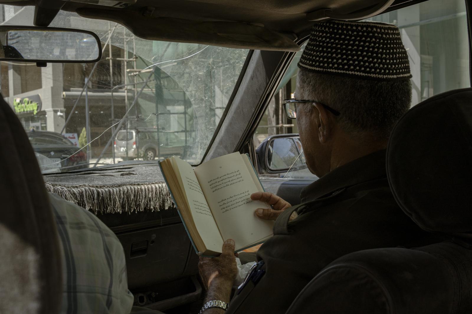 Hazar Jaf, an elderly Kurd, rea... an Iranian book while driving.
