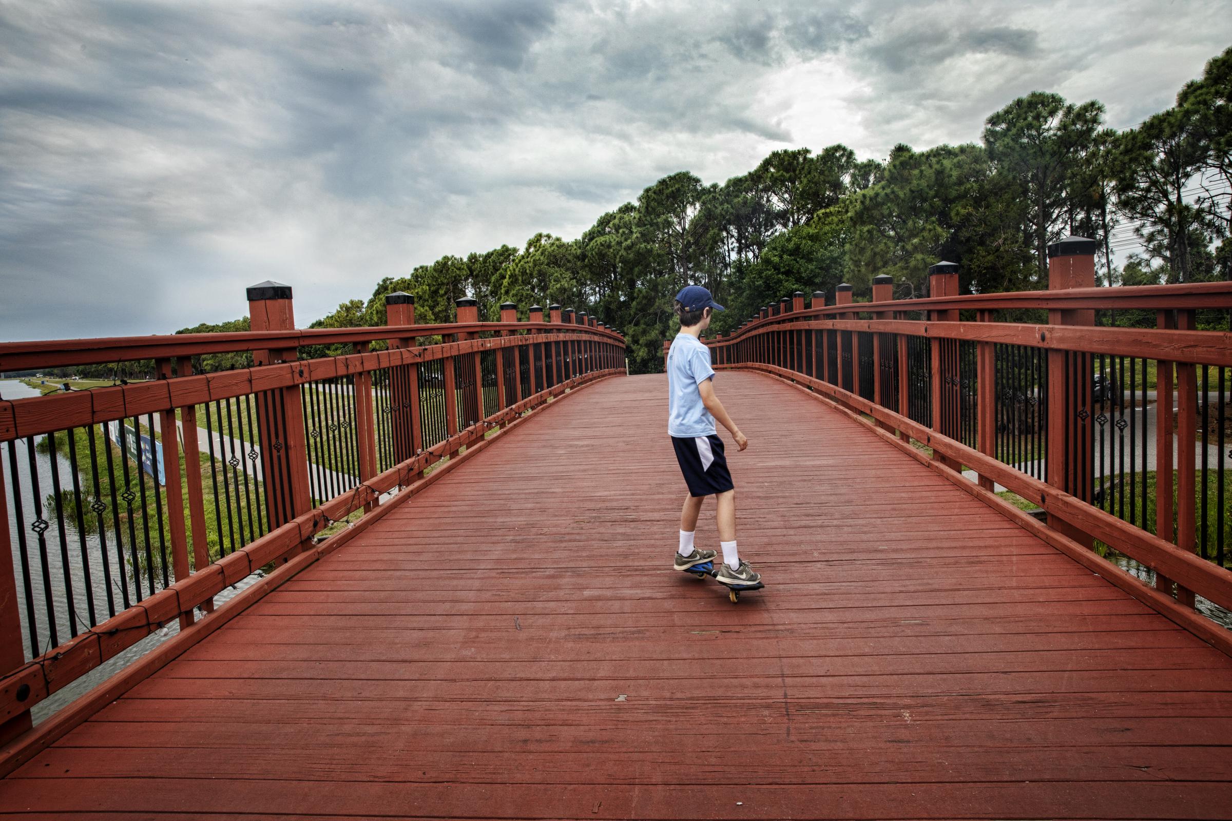 Growing Up - A young boy rides his skateboard across a bridge at...