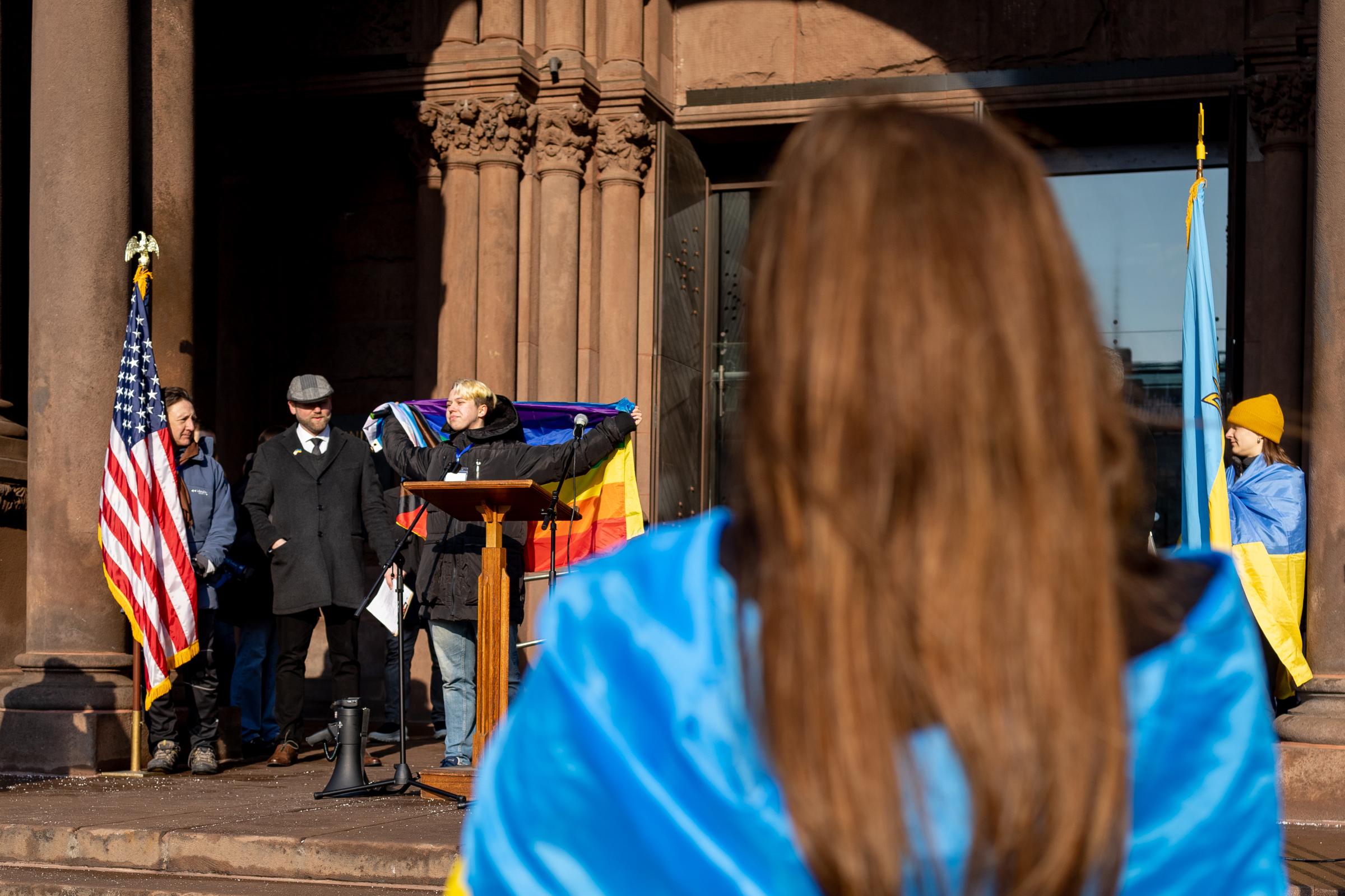 Demonstrators Gather at Copley Square in Support of Ukraine, Exactly a Year Since Russia's Invasion - A member of the LGBTQ community, Sashko Horokh displays their rainbow flag as demonstrators cheer...