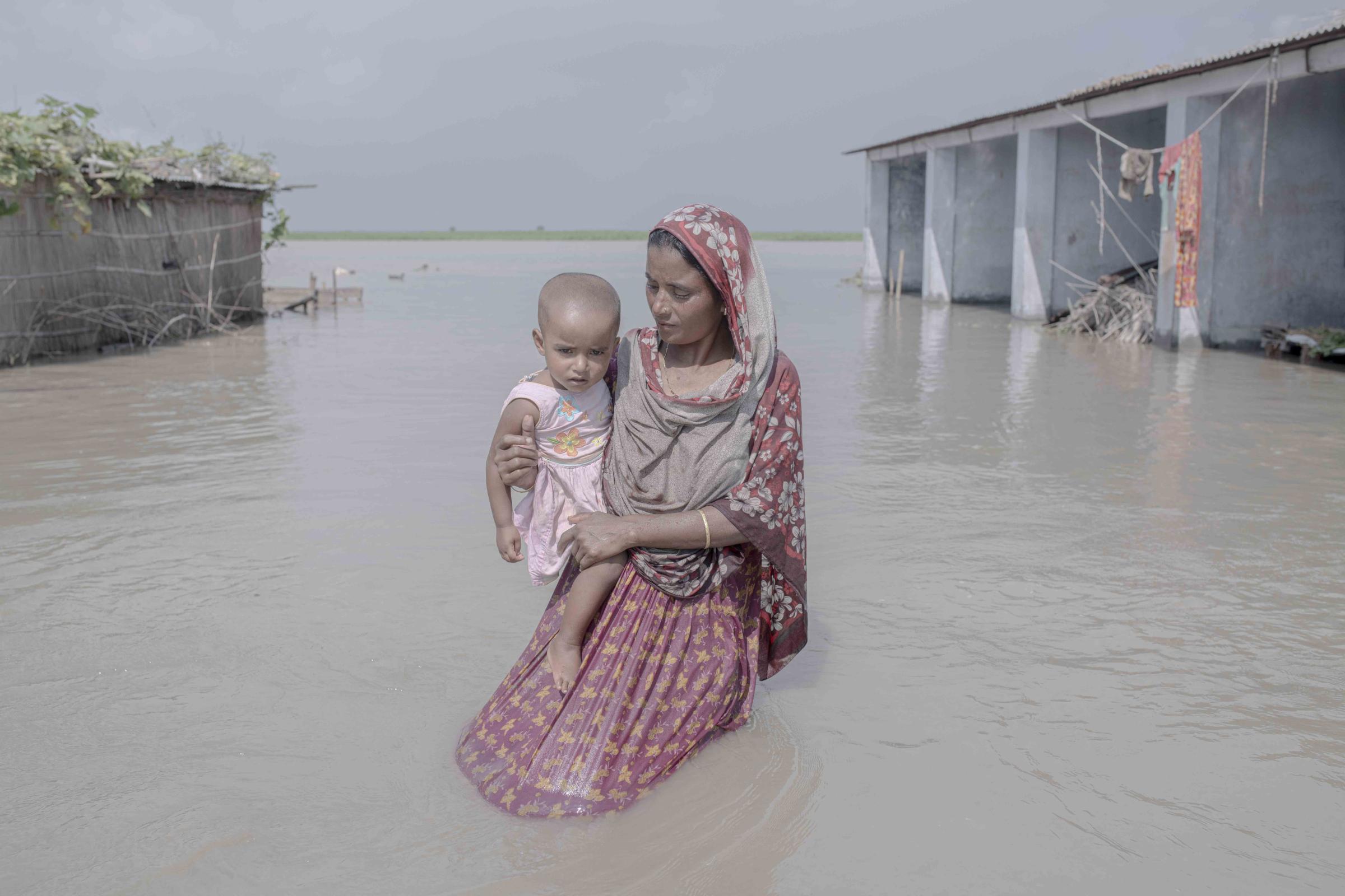 Flood Survival People -  Julekha Begum carries her child through a flooded street. 