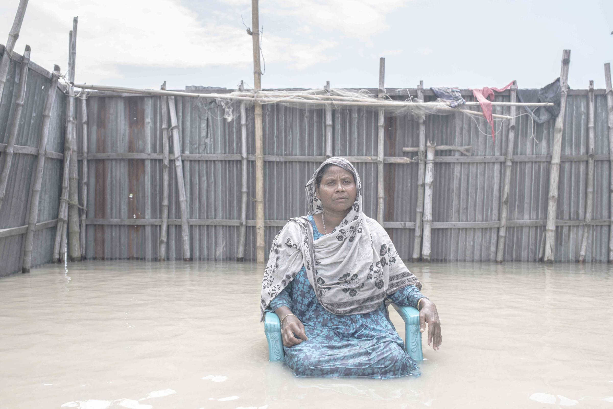 Flood Survival People -  Shefali Begum sits in front of their flooded house. 
