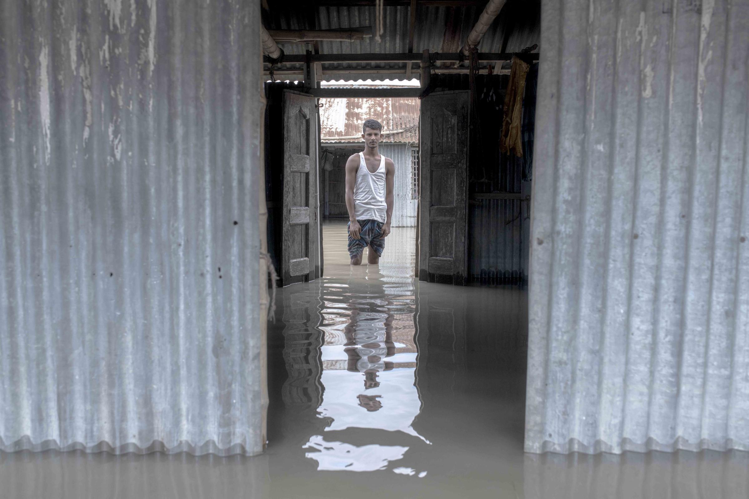Flood Survival People -  Akbor stands outside his flooded house. 