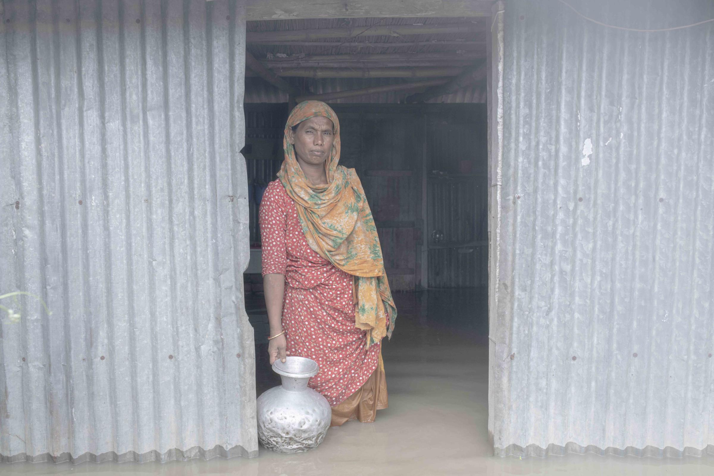 Flood Survival People -  Hena Begum stands in front of her flooded house with a...