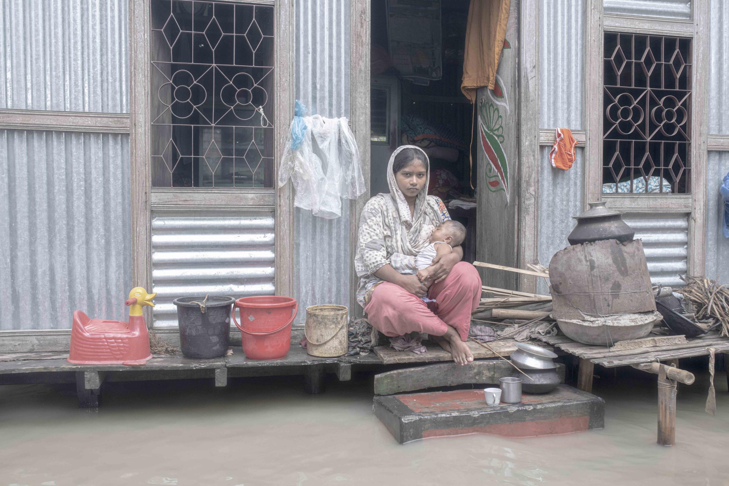 Flood Survival People -  A girl with her child sits in front of their flooded...