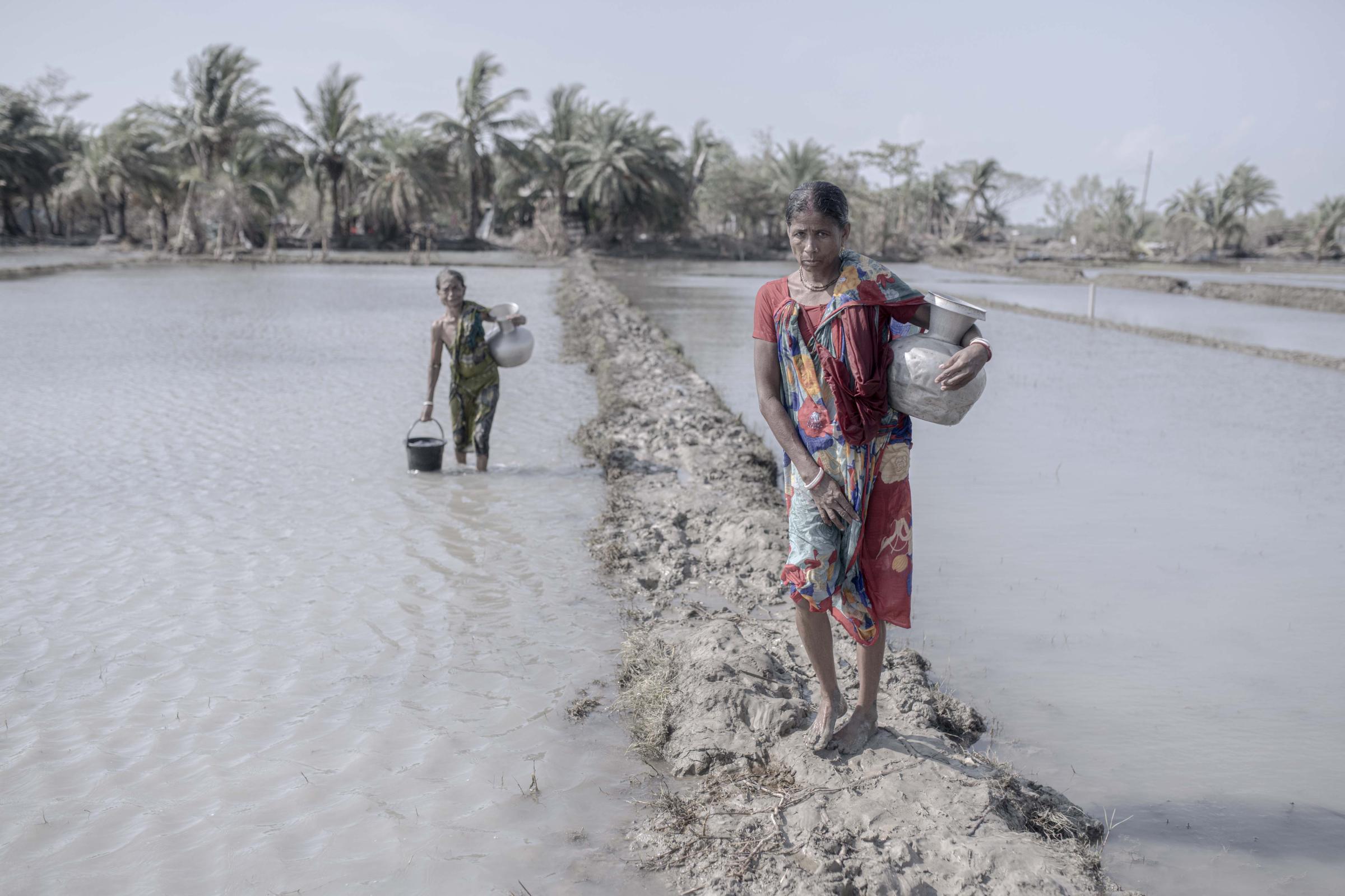 Salt Water's Roar -  Women walking on a flooded mud footpath during the...