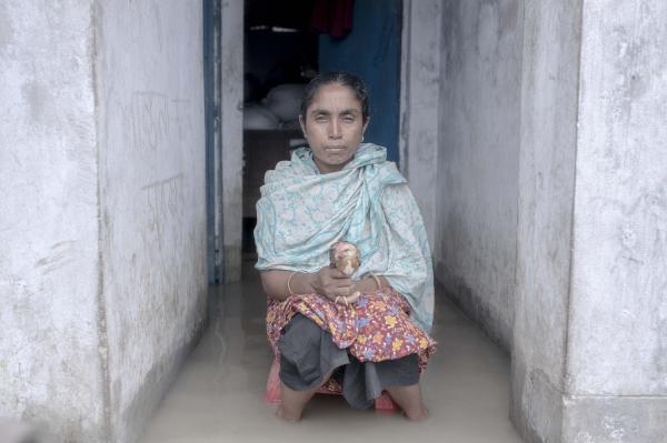 Image from Flood Survival People -  A woman with her pet sits in front of her flooded house. 