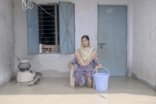 Image from Flood Survival People -  Anwara Begum sits in front of her flooded house. 