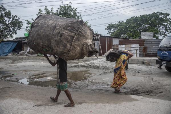Dangerous job of recycling - A recycling man in Dhaka&#39;s Baunya-Badh slum carries a huge, heavy bag of different typed...