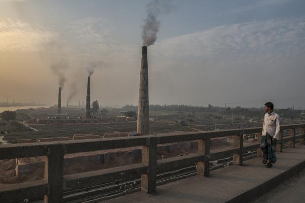 Dangerous job of recycling - A man walks on a bridge, in the background a brick factory generating carbon dioxide. Bangladesh...