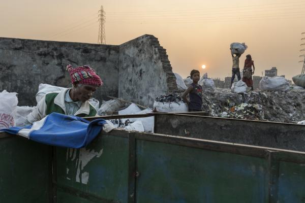 Dangerous job of recycling - A man, a child and a couple in the background search for materials to recycle in an open dump in...